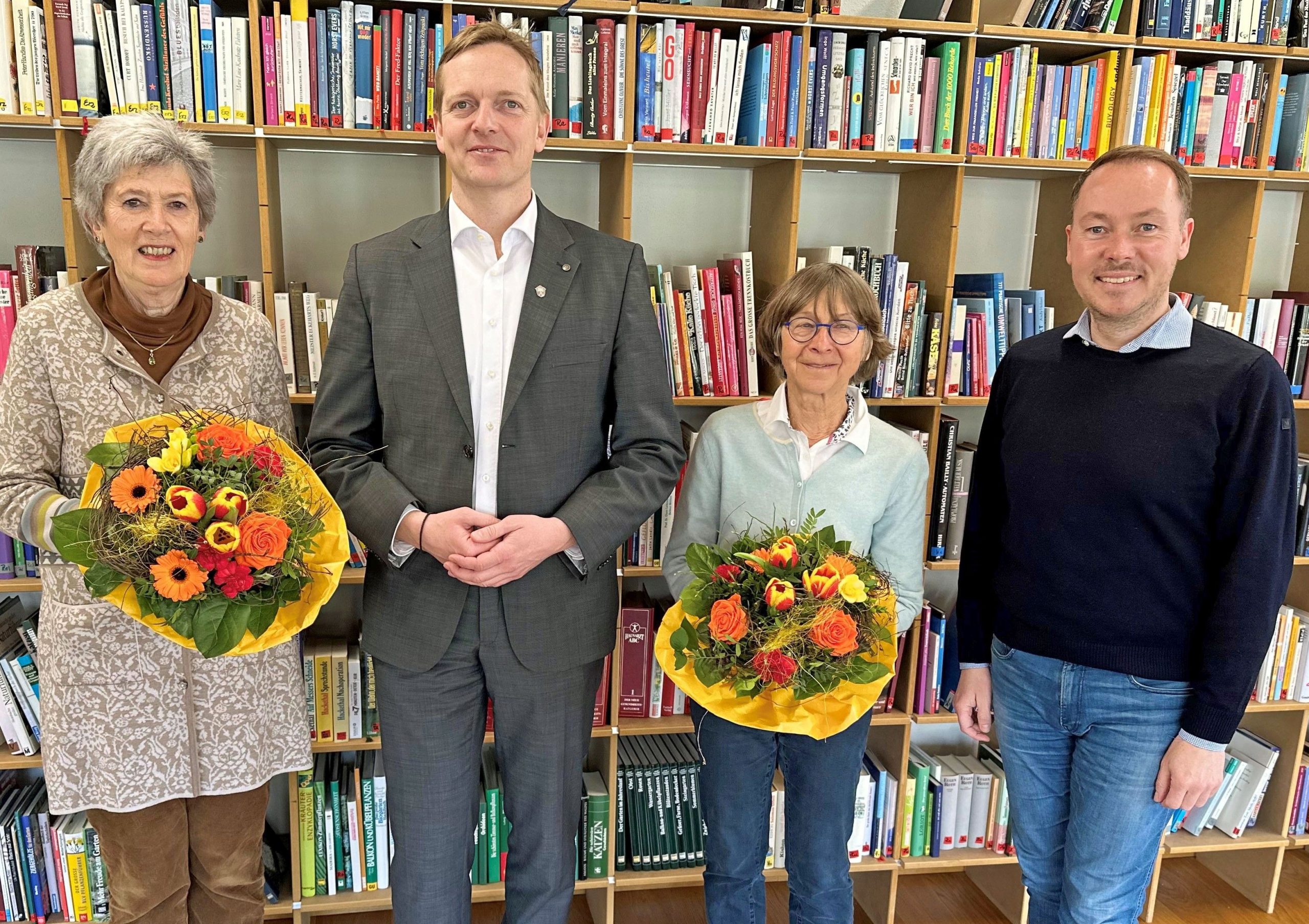 von links Ute Schwartz, Aschaus Bürgermeister Simon Frank, Christel Lenhard und Tourismuschef Herbert Reiter vor einer Wand mit Büchern. Die beiden Damen halten je einen bunten Blumenstrauß in den Händen