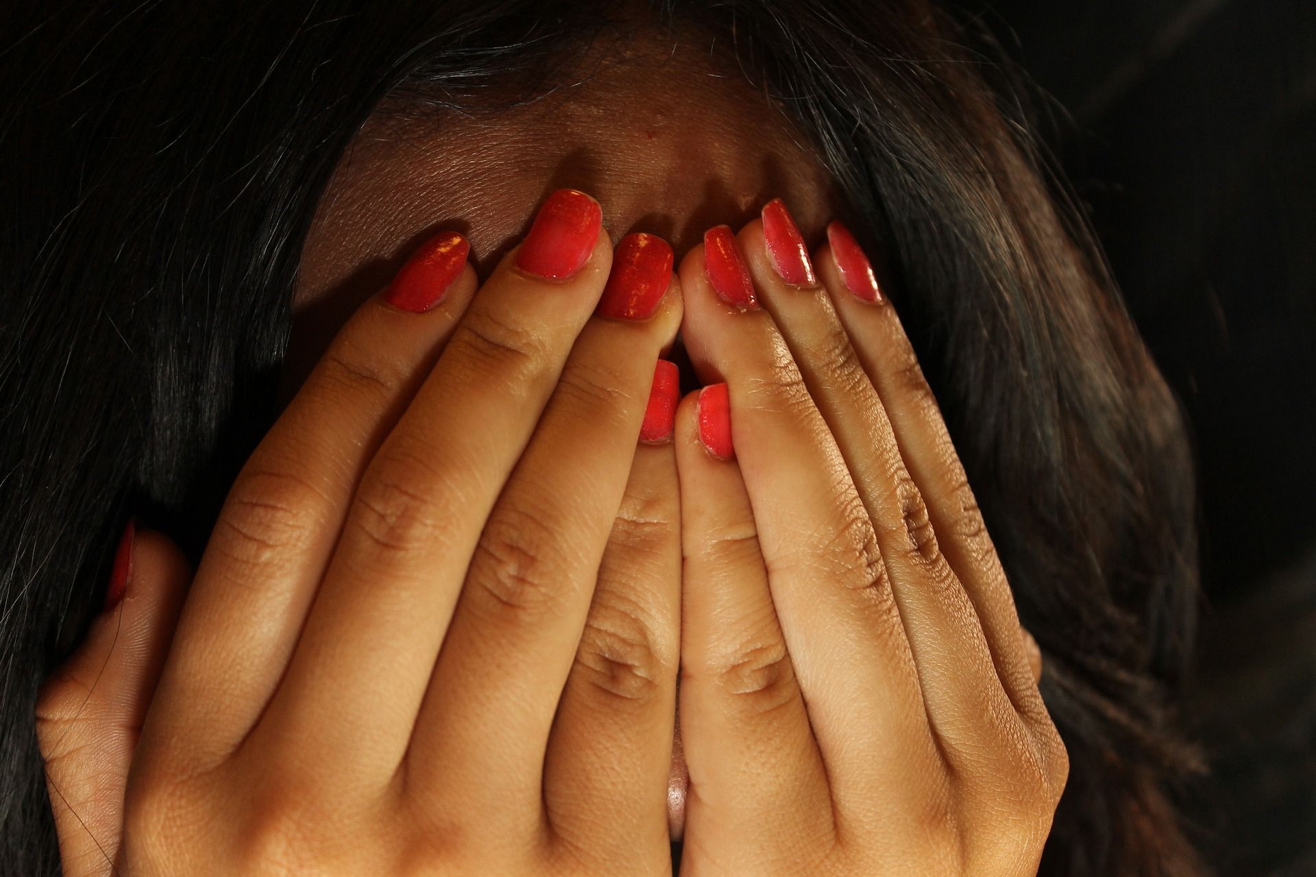 Hände mit roten Fingernägeln vor dem Gesicht einer Frau geschlagen