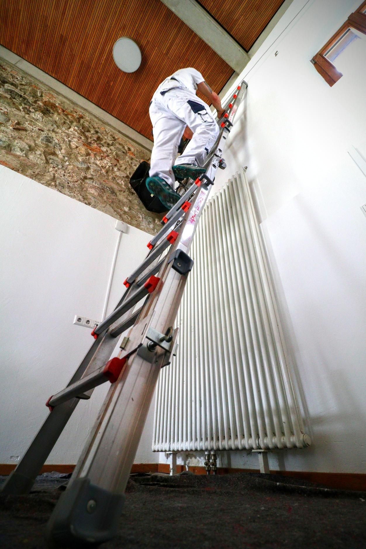 Maler Mario Erbertseder klettert im Jugendzentrum ChillMill in Rosenheim auf eine Leier um die Wand zu streichen