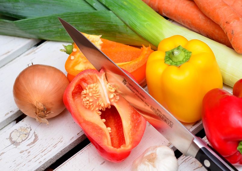 Paprika und anderes Gemüse liegen auf einem weißen Holztisch, außerdem ein Messer zum Schneiden