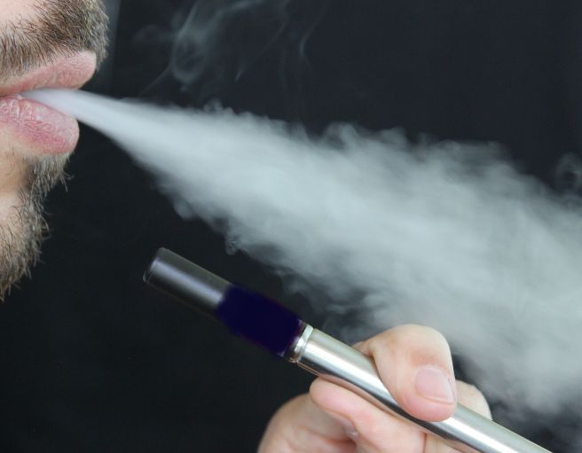 Mann raucht E-Zigarette. Ausschnitt von Mund, Zigarette, Hand und Rauch