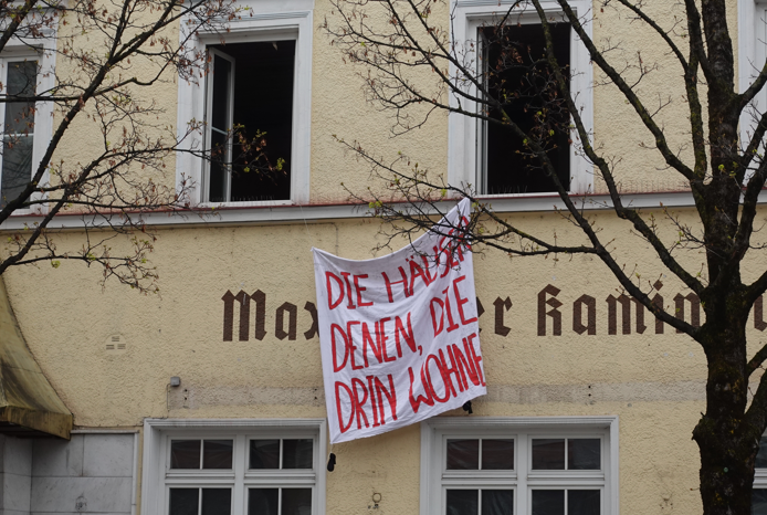 Schild mit roter Schrift hängt bei geöffneten Fenstern bei der Hausbesetzung des ehemaligen Hotels Goldener Hirsch in Rosenheim heraus. Foto: Archiv Innpuls.me
