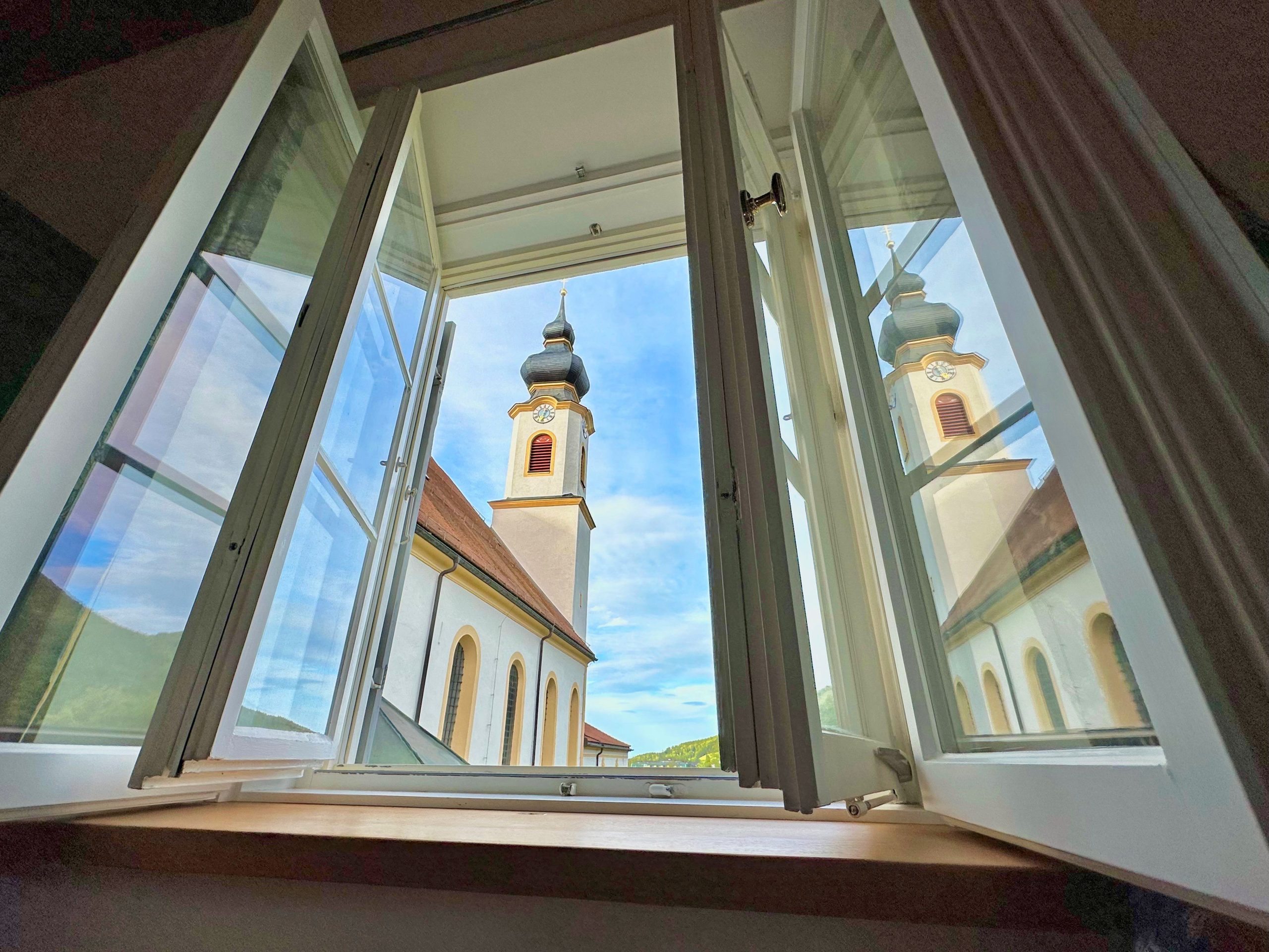 Die katholische Aschauer Pfarrkirche spiegelt sich in einem geöffneten Fenster. Foto: H. Reiter