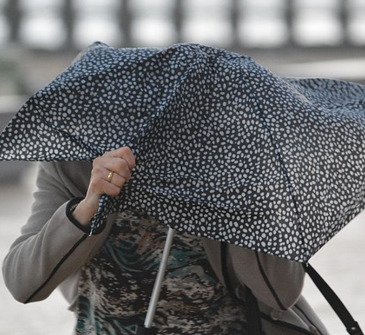 Frau unter Schirm, der sich im Wind verbiegt.