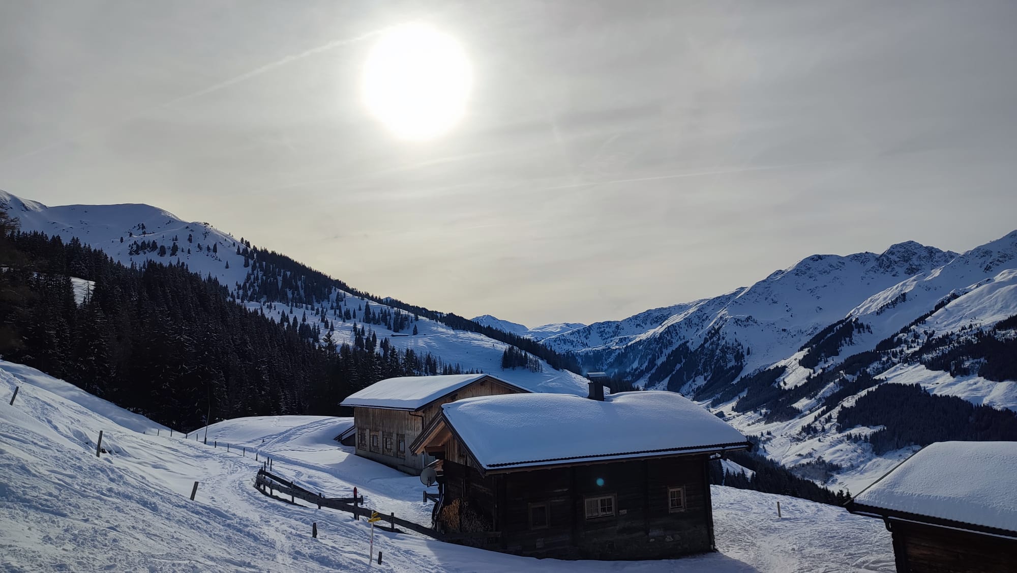 Sonne steht über einer schneebedeckten Hütte in den Bergen