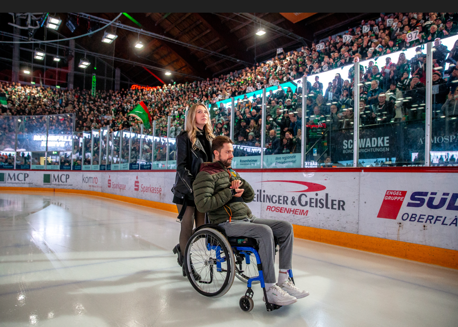 Mike Glemser im Rollstuhl mit Freundin auf dem Eis wird von Zuschauern im Rofa-Eisstadion in Rosenheim bejubelt. Foto: Copyright Peter Lion / Ludwig Schirmer