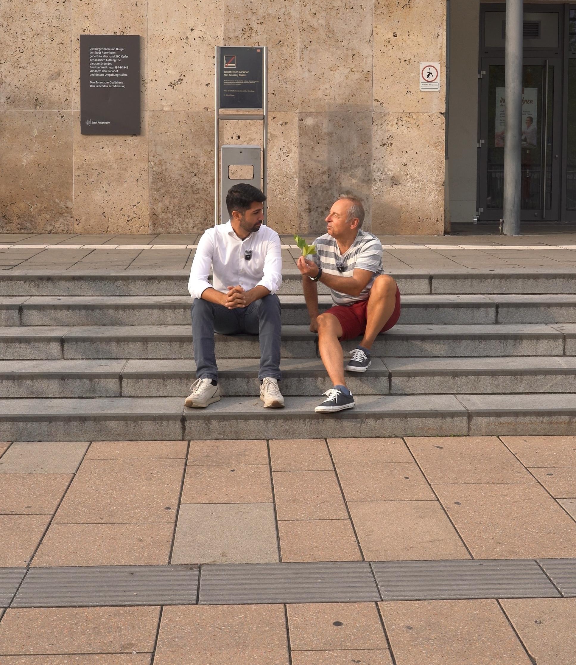 Foto Bahnhofsvorplatz SPD-Fraktionsvorsitzender Abuzar Erdogan (links) und SPD-Stadtrat Robert Metzger auf den Stufen sitzend zum Bahnhof Rosenheim. Foto: Copyright SPD Rosenheim
