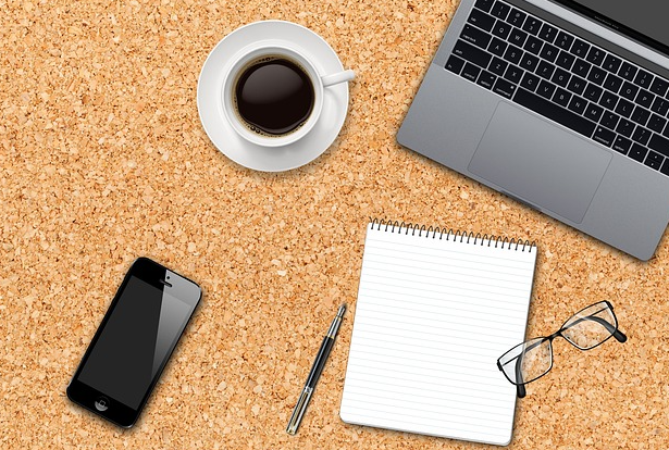 Wirtschaft Laptop, Kaffeetasse, Handy, Block, Brille und Stift auf Korkunterlage. Foto: re