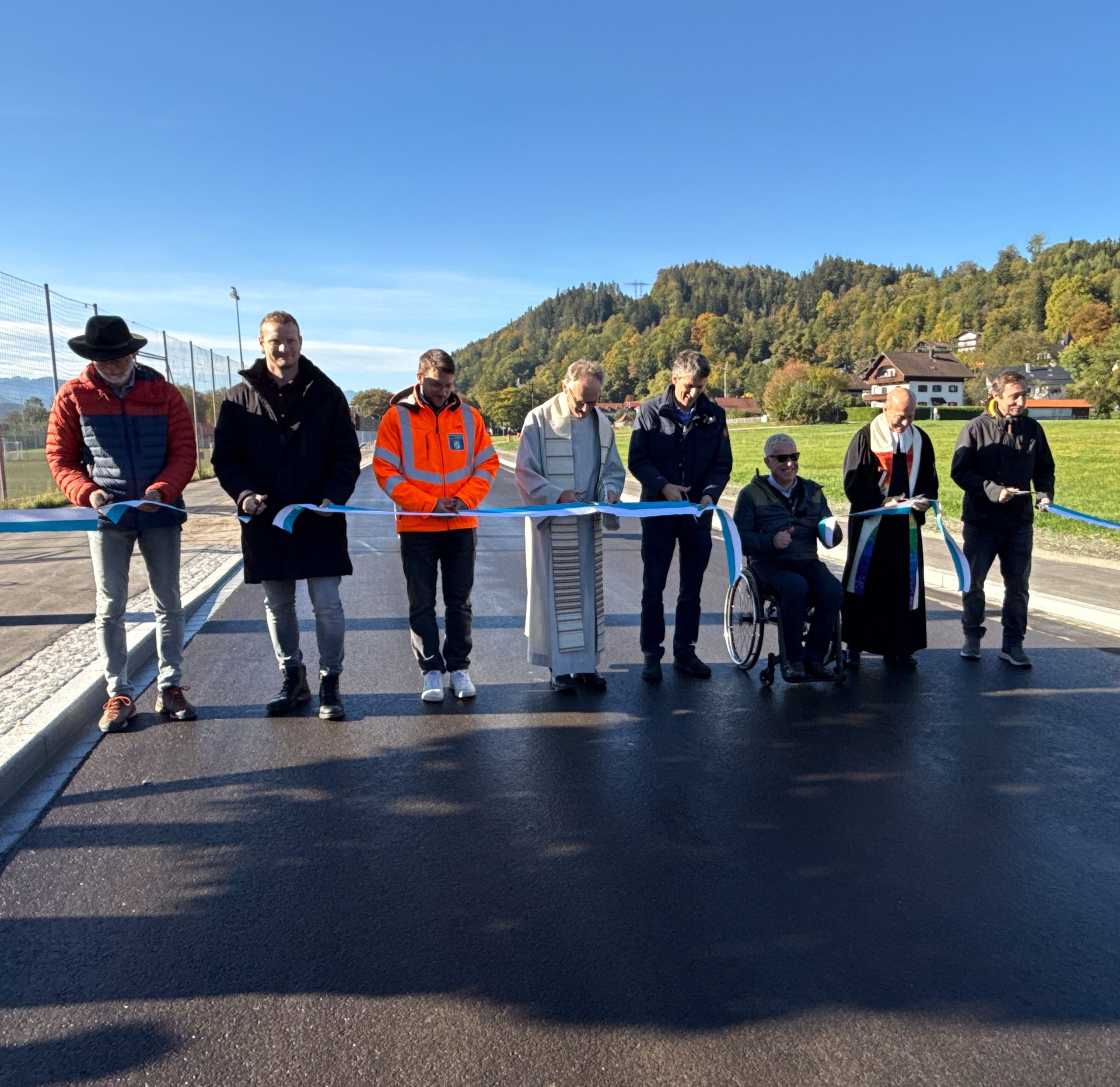 PM-65_2026-10-16_Pressesfoto-03 Erinnerungsfoto auf der neuen Straße (von links): Roland Bründl, Projektleiter am Staatlichen Bauamt Rosenheim; Maximilian Moser, Pfeiffer Baugesellschaft mbH; Alexander Eisner, Abteilungsleiter am Staatlichen Bauamt Rosenheim; Pfarrer Hans Huber (kath.); Dr. Hermann Streicher, Bereichsleiter Straßenbau am Staatlichen Bauamt Rosenheim; Hajo Gruber, 1. Bürgermeister der Gemeinde Kiefersfelden; Pfarrer Günter Nun (ev.); Andreas Horn, Gemeinde Kiefersfelden. Foto: Copyright Staatliches Bauamt Rosenheim